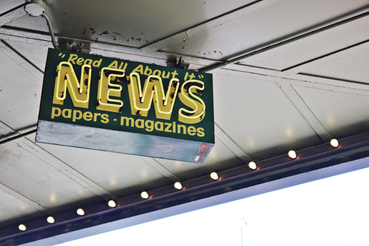 From below of illuminated signboard with news papers magazines inscriptions hanging on metal ceiling on street