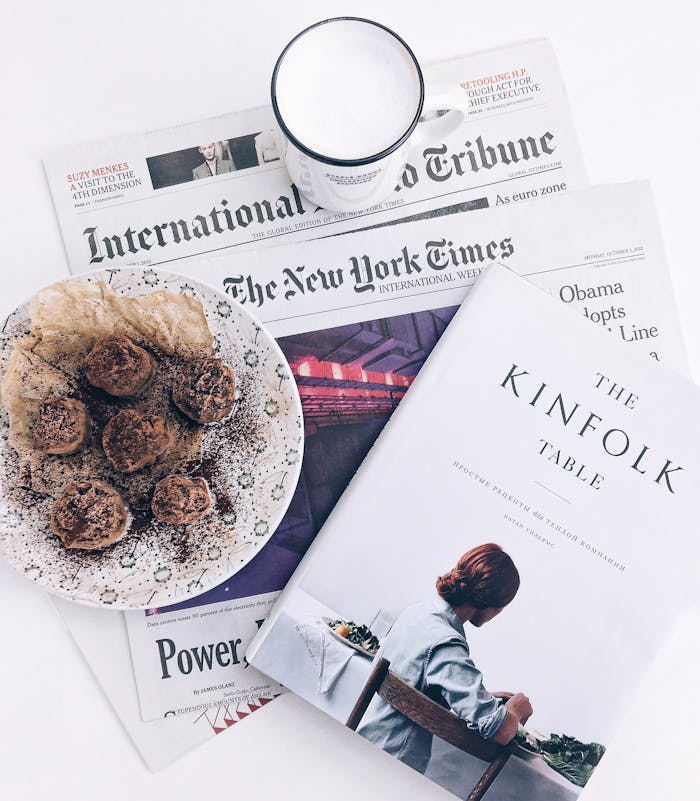 A flat lay of a breakfast scene with coffee, pastries, and newspapers, evoking a relaxed morning vibe.